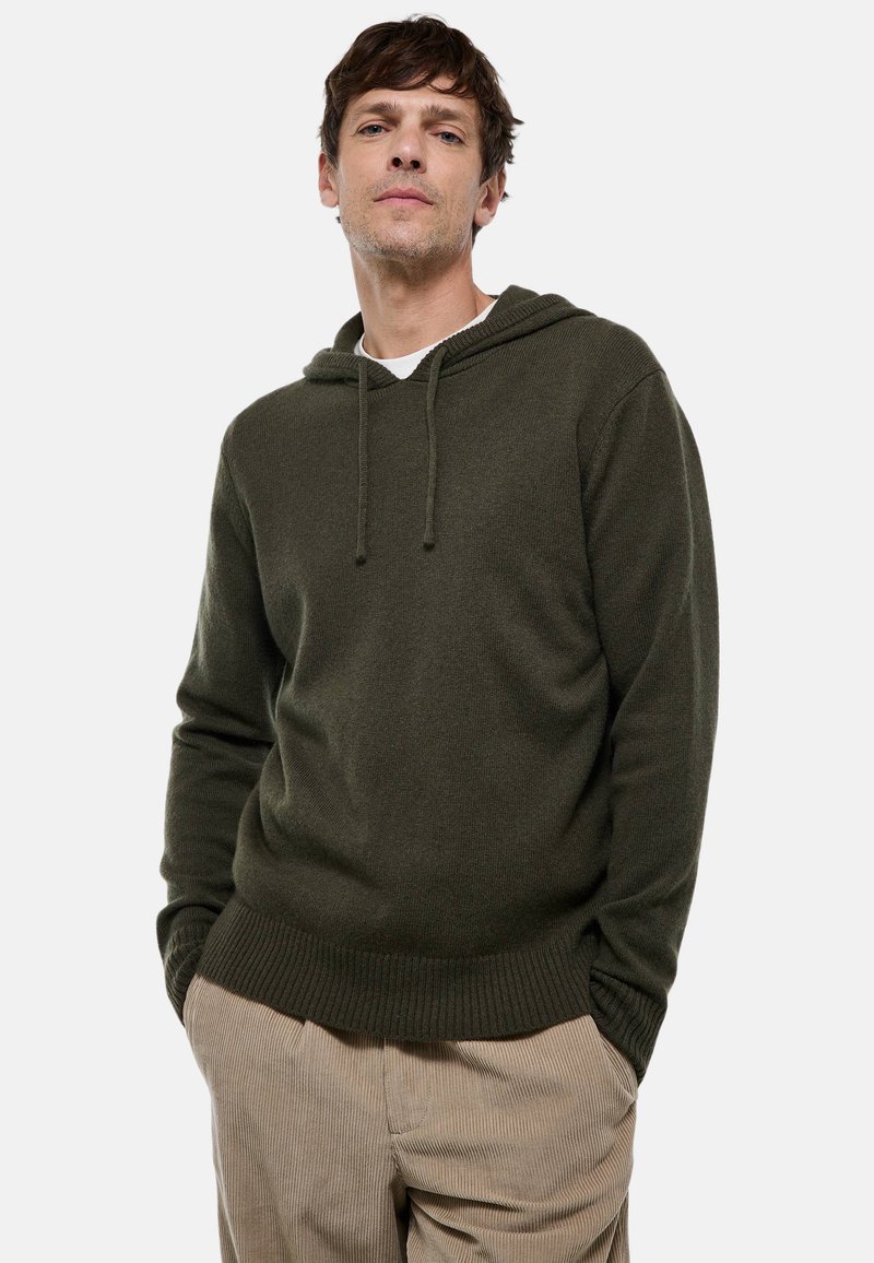 Haut à capuche en pull-over vert foncé en tissu doux, avec une capuche à cordon de serrage et des poignets côtelés. Associé à un pantalon en velours côtelé beige clair.
