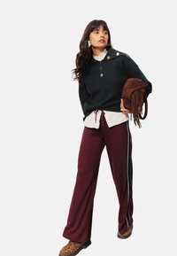 Pull overdimensionné bleu marine avec des boutons dorés, superposé à une chemise à carreaux blancs. Pantalons larges bourgogne avec des rayures latérales, associés à des bottes à imprimé léopard.