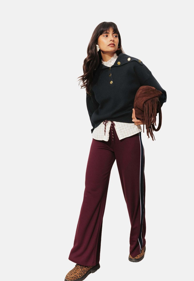 Pull overdimensionné bleu marine avec des boutons dorés, superposé à une chemise à carreaux blancs. Pantalons larges bourgogne avec des rayures latérales, associés à des bottes à imprimé léopard.