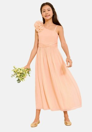 Girl in a peach one-shoulder dress with floral detail, holding a bouquet of white flowers, wearing gold ballet flats and a bracelet.