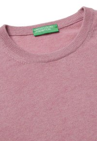 Różowy sweter z okrągłym dekoltem, wykonany z miękkiej tkaniny, z zieloną metką z napisem "United Colors of Benetton" wszytą w dekolt.