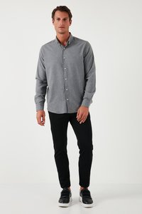 Grijze button-up shirt met lange mouwen, een kraag en witte knopen, gecombineerd met zwarte slim-fit broek en zwarte instappers.