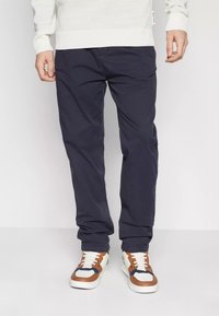 Chinos blu navy in cotone, con vestibilità dritta, dotati di tasche laterali e passanti per cintura, abbinati a sneaker bianche e marroni.