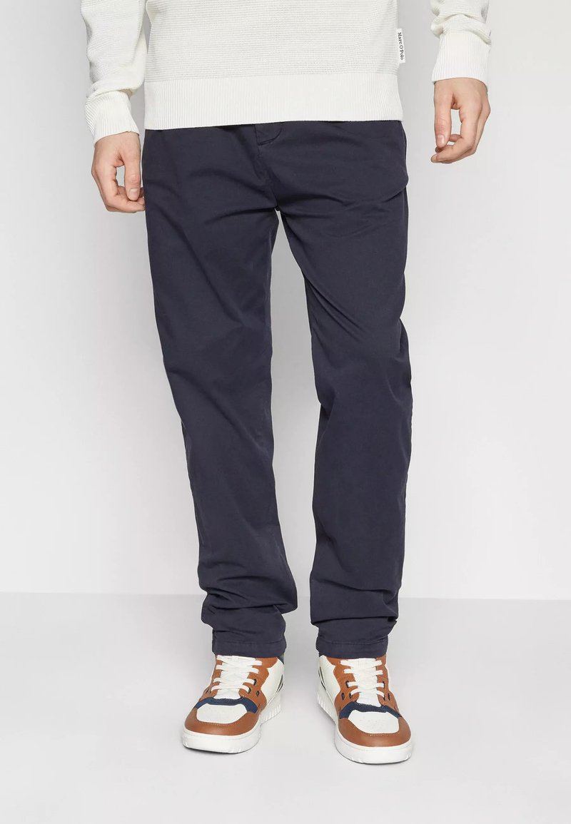 Chinos blu navy in cotone, con vestibilità dritta, dotati di tasche laterali e passanti per cintura, abbinati a sneaker bianche e marroni.