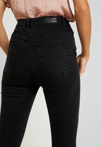 Mustat farkut, joissa on kapea istuvuus, korkea vyötärö ja kaksi takataskua. Kangas on hieman joustavaa mukavuuden vuoksi.