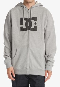 Hoodie zippé gris en fleece doux, avec un grand logo noir sur le devant, une capuche avec cordon de serrage et des poches avant.