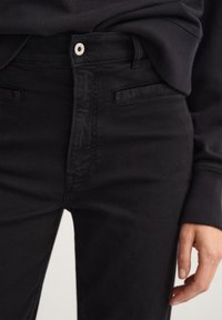 Jeans de mezclilla negra con un diseño ajustado, que cuentan con un botón superior plateado, bolsillos frontales y una textura suave.