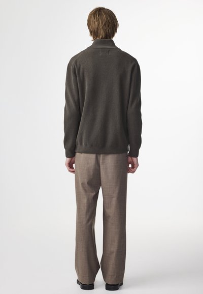 Pull en maille gris foncé à col montant, associé à un pantalon sur mesure beige clair. La tenue a une coupe décontractée et des détails de design minimaux.