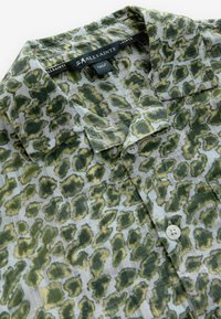 Camicetta a maniche corte con un motivo a stampa leopardata verde e grigia, realizzata in tessuto leggero, con colletto aperto e chiusura a bottoni.
