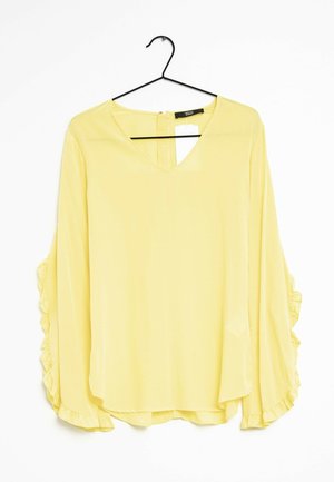 Gele blouse met lange, gerimpelde mouwen. V-halslijn en sleutelgatopening aan de achterkant. Lichtgewicht stof valt zachtjes om het lichaam.