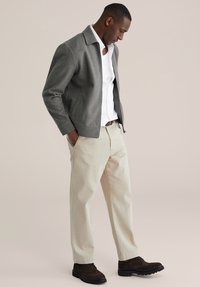 Szara wełniana marynarka na białej koszuli, zestawiona z beżowymi spodniami i ciemnobrązowymi butami. Strój charakteryzuje się czystymi liniami i dopasowanym krojem.