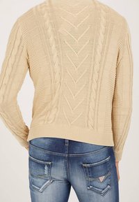 Beige kabelstickad tröja med ribbad nederkant, bärs tillsammans med blå blekta jeans med bakfickor och subtil förslitning.