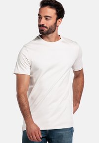 Weißes T-Shirt mit kurzen Ärmeln aus Baumwolle. Rundhalsausschnitt mit glatter Textur. Kombiniert mit blauen Jeans, die einen lässigen Look zeigen.