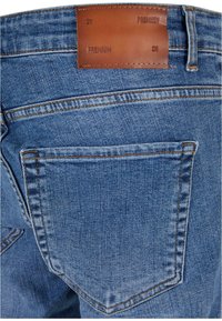 Modre jeans hlače iz denima z gladko teksturo, zadnjimi žepi in rjavim usnjenim trakcem na pasu, označenim z "PREMIUM."