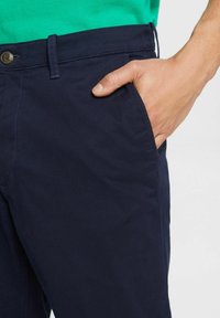 Jūras spēku stila chinos bikses, kas izgatavotas no kokvilnas ar gludu tekstūru, piedāvā priekšējo kabatu un brūnu pogu aizdari jostasvietā.