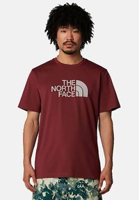 Camiseta de manga corta color burdeos, hecha de una tela suave, con un gran logo gris de "The North Face" en el pecho. Corte casual.