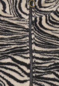 Černá a krémová fleecová bunda s pruhovaným vzorem zebry, která má přední zip a kulatý úchyt zipu. Měkký a hebký materiál.