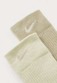 Calcetines de punto en tonos marrón claro y verde claro con sutiles logotipos de Nike. Con puños acanalados y textura suave. Cada uno presenta un color neutro distintivo.