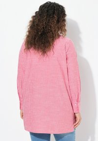 Camicia a maniche lunghe a righe rosse e bianche, con una vestibilità comoda, polsini con bottoni e un retro più lungo. Tessuto in cotone con una texture morbida.