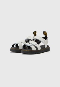 Witte sandalen met meerdere zwarte banden, open neus, voorzien van een gestructureerde zwarte zool en gele trekbanden op de hak.