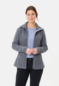 Giacca in pile grigia con colletto strutturato, zip frontale e cordini regolabili. Indossata sopra una camicia azzurra chiara.