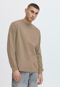 Langärmliges, taubefarbenes T-Shirt aus weichem Stoff mit Rundhalsausschnitt und gerippten Bündchen, kombiniert mit hellgrauen Jeans, die eine lockere Passform zeigen.