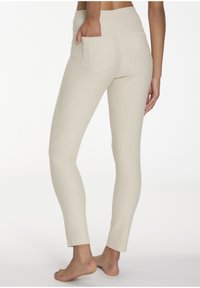 Beige Leggings mit einer taillierten Passform, hohem Bund und zwei Gesäßtaschen, mit glatter Textur und leicht verkürzter Länge.