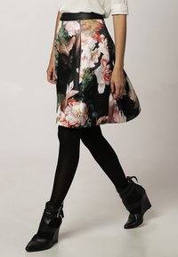 Jupe trapèze à imprimé floral noire, ornée de fleurs éclatantes en rose et blanc, fabriquée dans un matériau brillant. Associée à des bottines compensées noires.