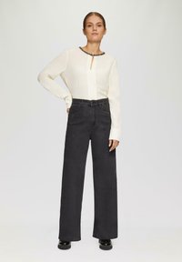Haut à manches longues ivoire avec un décolleté en trou de serrure et des accents en perles noires, associé à un jean noir à taille haute et jambes larges comportant des embellissements subtils.