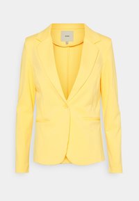 Blazer jaune sur mesure avec un revers cranté, une fermeture à un bouton et deux poches avant. Confectionné dans un tissu lisse et léger.