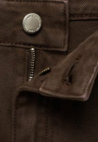Rjav denim material vsebuje kovinsko pritisno gumb in zadrgo. Texturirana površina s subtilnim črtastim vzorcem, trdni šivi in dodatna žepna zasnova.