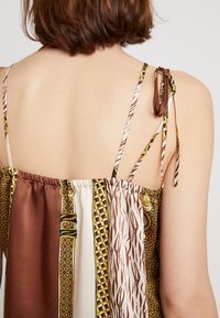 Top in satin con una combinazione di motivi animali e geometrici nei toni del marrone, bianco e giallo. Presenta spalline regolabili con nodo e una schiena arricciata.
