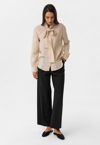 Beige blouse met een geknoopte kraag, lange mouwen en een gestructureerde afwerking, gecombineerd met zwarte wijde broek en zwarte flats. Eenvoudig ontwerp.