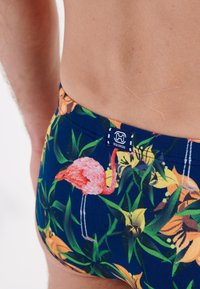 Marineblaue Schwimmshorts mit pinken Flamingos und Blumenmuster. Mit elastischem Bund und Logoetikett. Material wirkt glatt und dehnbar.