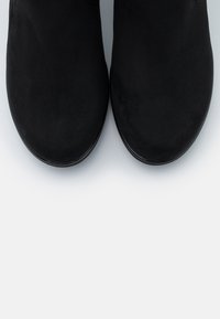 Paire de bottines en daim noir à bouts arrondis sur une surface gris clair, vue de dessus.