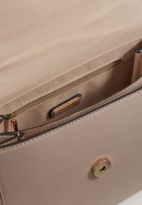 Interior de un bolso de cuero beige con un bolsillo con cremallera, acentos en hardware dorado y una textura suave, con una etiqueta de marca sutil.