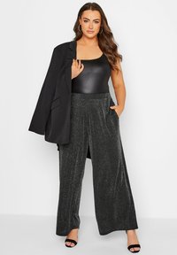 Svart åtsittande bodysuit, kombinerad med vida svart glittrande byxor med fickor. Strukturerad svart kavaj som hängs avslappnat över ena axeln.