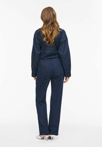 Granatowy zestaw w groszki, składający się z luźnej bluzki z długim rękawem oraz spodni o prostych nogawkach z elastycznym pasem. Tkanina wydaje się miękka.