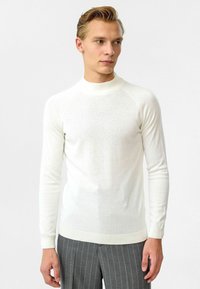 Witte lange mouw trui met een hoge hals, gemaakt van een gestructureerde brei-stof. Heeft ribgebreide manchetten en zoom, en is ontworpen met een getailleerde pasvorm.