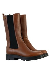 Un par de botas de cuero marrón hasta la mitad de la pantorrilla con paneles laterales elásticos negros y suelas de goma negra gruesa, inclinadas hacia la derecha sobre un fondo blanco.