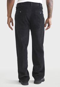 Pantalon en velours côtelé noir avec une texture à côtes verticales, deux poches arrière et une coupe décontractée. La ceinture comprend des passants pour ceinture pour un ajustement.