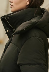 Fekete puffertakaró, magas gallérral, steppelt mintázattal, fényes anyaggal és ezüst cipzárral. Puha, texturált felület.