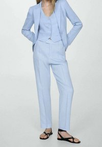 Completo tre pezzi di color blu chiaro composto da un blazer aderente, un gilet bottonato e pantaloni su misura. Presenta una texture liscia e un design minimalista.