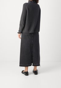 Oversized ciemnoszary sweter w prążki z wysokim kołnierzem, w połączeniu z długą czarną spódnicą dżinsową z postrzępionym dołem. Czarne buty slip-on.