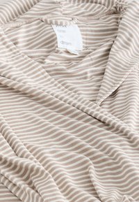 Weicher beige-weißer Stoff mit horizontalen Streifen und einem sichtbaren Etikett, auf dem steht "Nächstes Mal zu träumen."