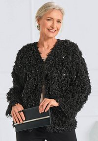 Schwarze, flauschige Jacke mit einem strukturierten Design und Pailletten. Sie hat lange Ärmel, einen runden Ausschnitt und wird mit einer schwarzen Clutch kombiniert.