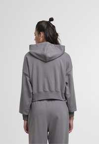 Sweat-shirt gris court en tissu doux avec capuche, manches larges et poignets côtelés. L'arrière présente une texture lisse sans motifs visibles.