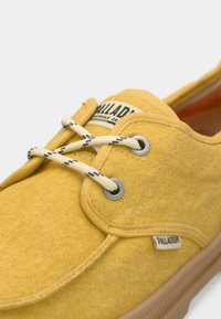 Κίτρινο πάνινο παπούτσι με γκρι πόρπες, κρεμ κορδόνια με μαύρες λεπτομέρειες και καφέ λαστιχένια σόλα. Ετικέτα με λογότυπο στην πλευρά.