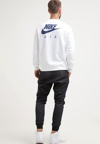 Witte sweatshirt met een marineblauw "Nike Air" logo op de achterkant, gecombineerd met zwarte taps toelopende joggers en witte sneakers. Gemaakt van katoen, casual pasvorm.