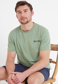 Light green cotton t-shirt with short sleeves and a crew neck, featuring a navy logo reading "EBB & FLOW" on the left chest.